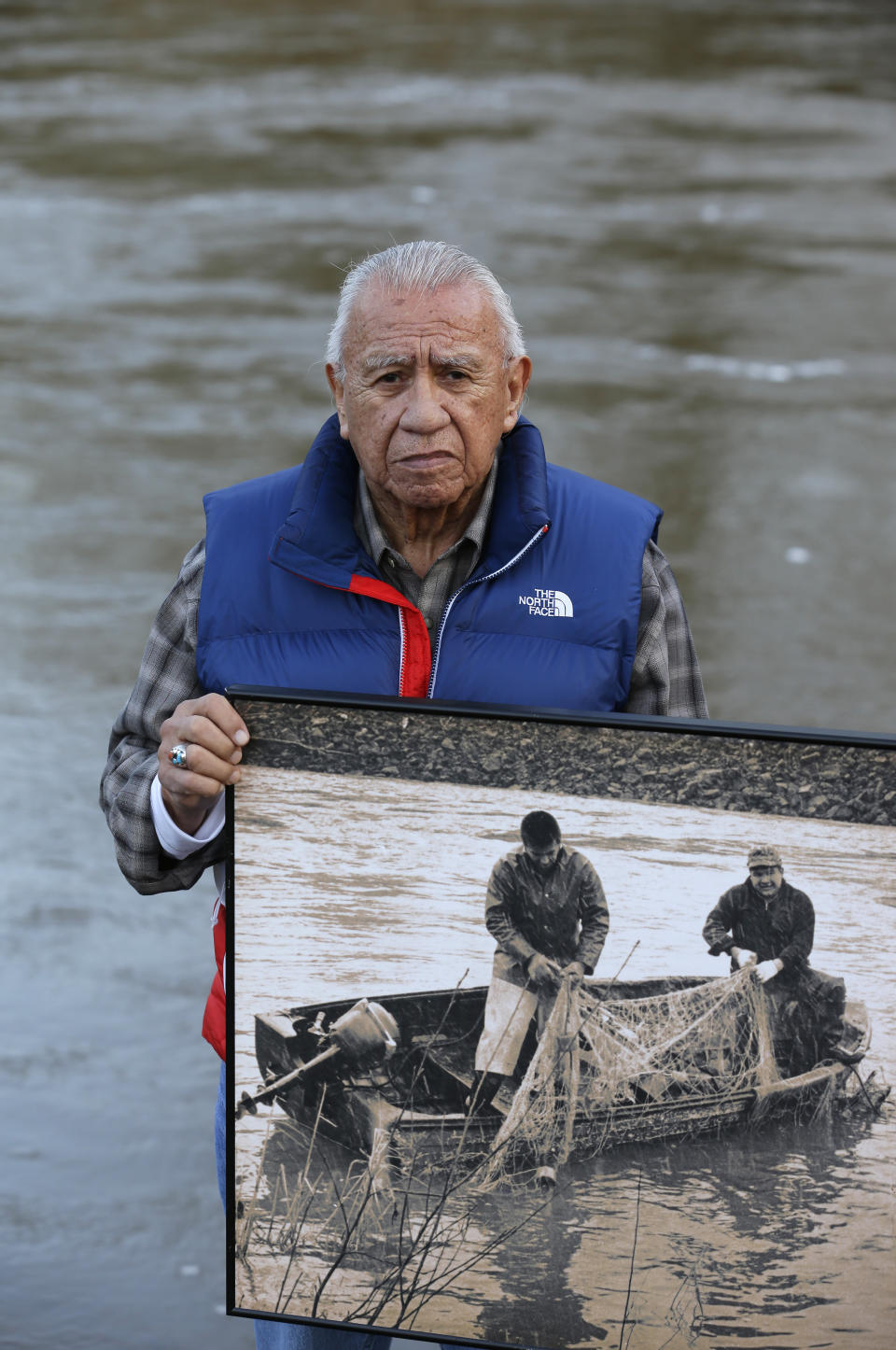 FILE - In this Monday, Jan. 13, 2014, file photo Billy Frank Jr., a Nisqually tribal elder who was arrested dozens of times while trying to assert his native fishing rights during the Fish Wars of the 1960s and '70s, poses for a photo while holding a late 1960s photo of himself, left, fishing with Don McCloud, near Frank's Landing on the Nisqually River in Nisqually, Wash. Gov. Jay Inslee on Wednesday, April 14, 2021, signed a measure that starts the process of honoring the late Frank, who championed treaty rights and protecting the environment with a statue at the U.S. Capitol. (AP Photo/Ted S. Warren, File)