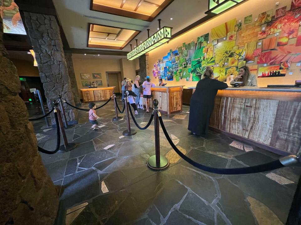 A hotel check-in desk with a colorful backdrop and people waiting to be checked in.