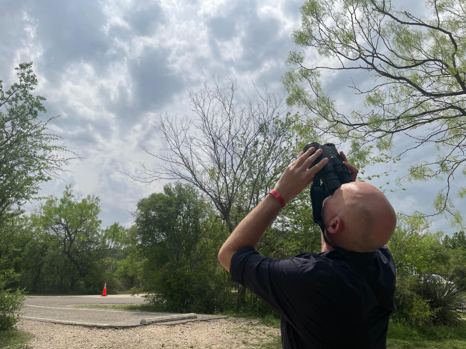 A bald man peers up through binoculars.