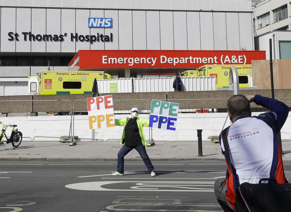 A woman holding up signs (PPE-Personal Protection Equipment) is photographed as she stands outside St Thomas' Hospital in central London as British Prime Minister Boris Johnson is in intensive care fighting the coronavirus in London, Tuesday, April 7, 2020. Johnson was admitted to St Thomas' hospital in central London on Sunday after his coronavirus symptoms persisted for 10 days. Having been in hospital for tests and observation, his doctors advised that he be admitted to intensive care on Monday evening. The new coronavirus causes mild or moderate symptoms for most people, but for some, especially older adults and people with existing health problems, it can cause more severe illness or death.(AP Photo/Kirsty Wigglesworth)