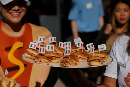 A woman gives away hot dogs from the vendor Walter's during the opening of an exhibit at Ellis Island highlighting the immigrant history behind the "Hot Dog" in New York City, U.S., June 28, 2017. REUTERS/Lucas Jackson