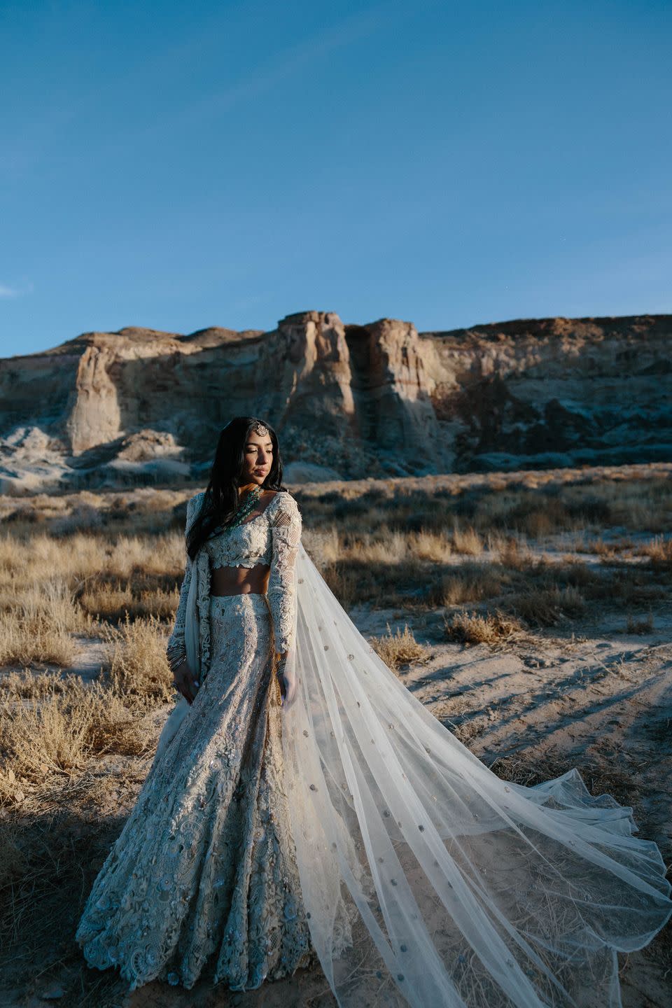 a person in a dress standing on a sandy beach with a rocky cliff behind the