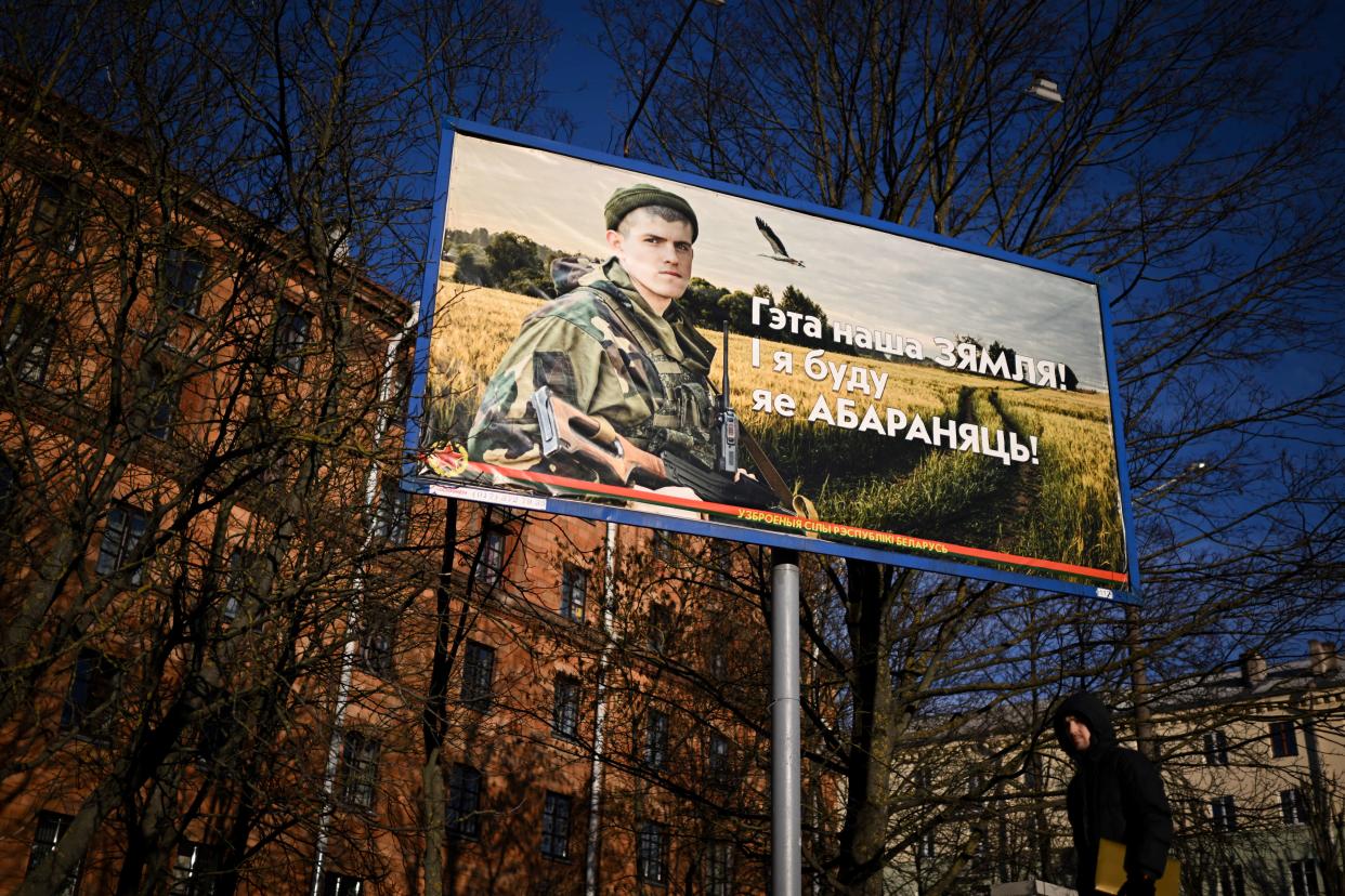 A man walks past a billboard depicting a service member holding a rifle in a cornfield, as a large raptor flies past.
