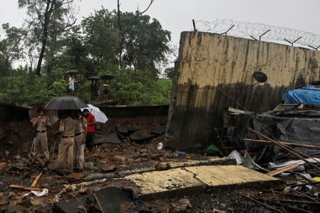 Police personnel stand among the debris after a wall collapsed on hutments due to heavy rains in Mumbai