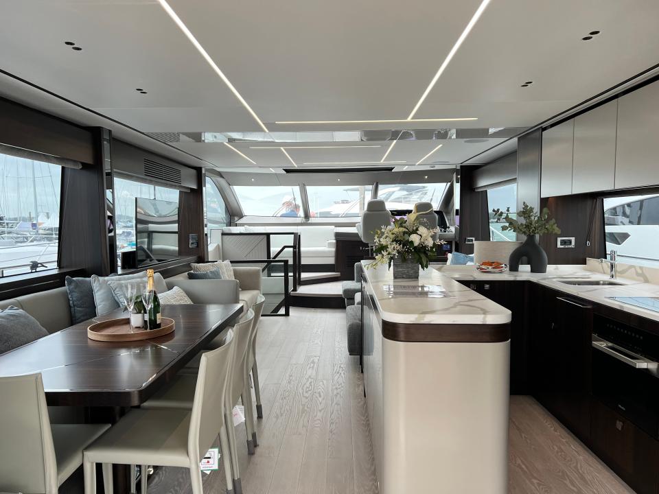 The main deck interior of a Sunseeker 76 yacht, with a kitchen, dining area, and living room all visible.
