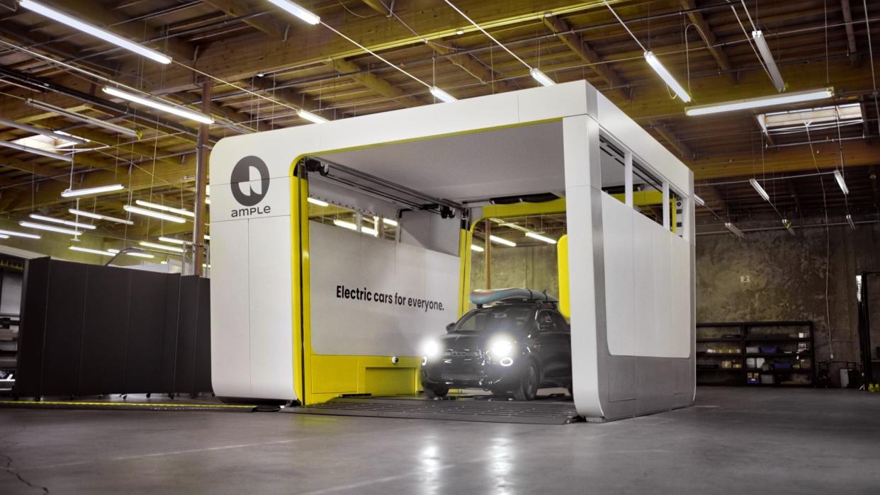 One of Ample's white battery-swapping stations sits in a warehouse with a small black car parked inside.