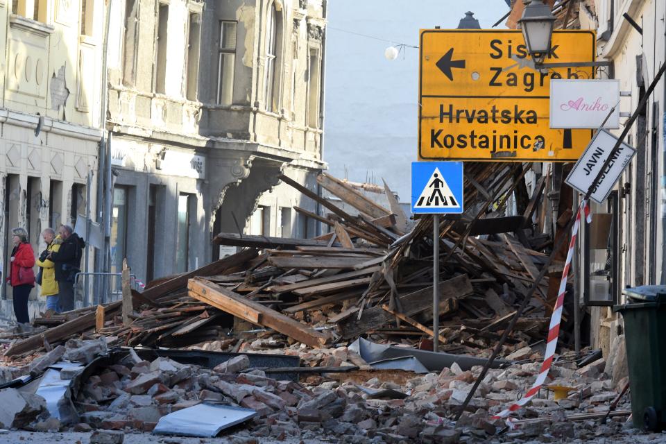 People stand next to the rubbles of damaged buildings in Petrinja, some 50kms from Zagreb, after the town was hit by an earthquake of the magnitude of 6,4 on December 29, 2020. - The tremor, one of the strongest to rock Croatia in recent years, collapsed rooftops in Petrinja, home to some 20,000 people, and left the streets strewn with bricks and other debris. Rescue workers and the army were deployed to search for trapped residents, as a girl was reported dead. (Photo by DENIS LOVROVIC / AFP) (Photo by DENIS LOVROVIC/AFP via Getty Images)