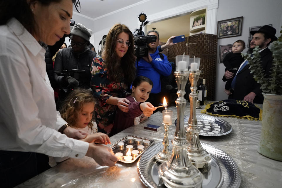 Members of the Chabad of Evanston, Ill., Yehudis Hecht, center, and her daughter Chana, and Maayan Hill, left, and her daughter Emilia, where Judith Raanan attended, light candles to mark the beginning of Shabbat on Friday, Oct. 20, 2023, in Evanston. Raanan and her daughter Natalie were released Friday from their captivity in Gaza. (AP Photo/Charles Rex Arbogast)