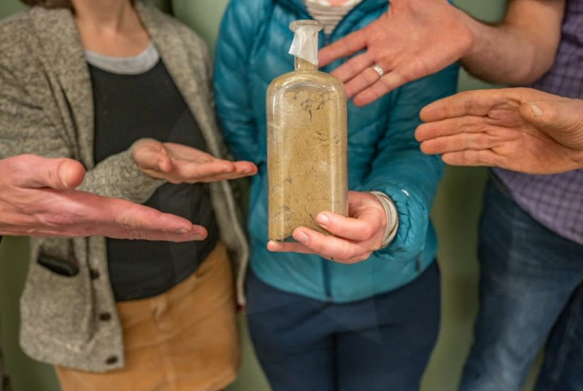 Five different researchers showcase a small glass bottle filled with sandy soil.