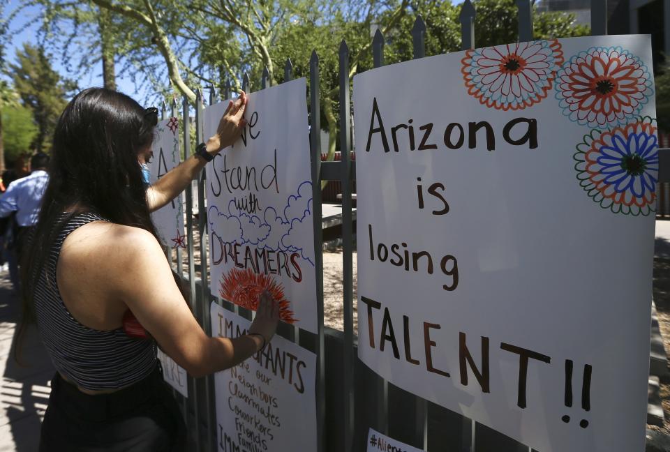 Deya Garcia, Deferred Action for Childhood Arrivals recipient, tapes up a poster in front of the U.S. Immigration and Customs Enforcement building during a during a news conference after the U.S. Supreme Court ruled on the DACA program Thursday, June 18, 2020, in Phoenix. The U.S. Supreme Court ruled President Donald Trump improperly ended the program that protects immigrants brought to the country as children and allows them to legally work, keeping the people enrolled in DACA. (AP Photo/Ross D. Franklin)