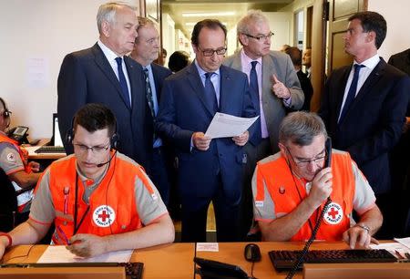 French President Francois Hollande (C) reads a document as he stands between Prime Minister Manuel Valls (R) and Foreign Minister Jean-Marc Ayrault (L) during a visit to the Interministerial Victim Support Unit (CIAV) at the Foreign Ministry in Paris, France, July 16, 2016. REUTERS/Matthieu Alexandre/Pool