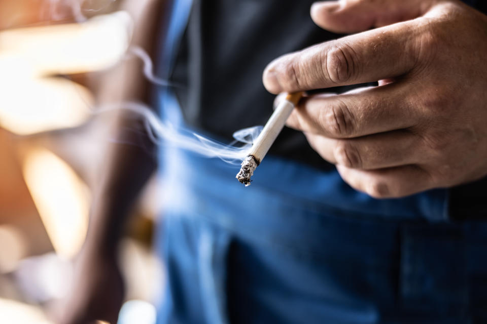 Detail of a man holding a smoking cigarette in his hand.