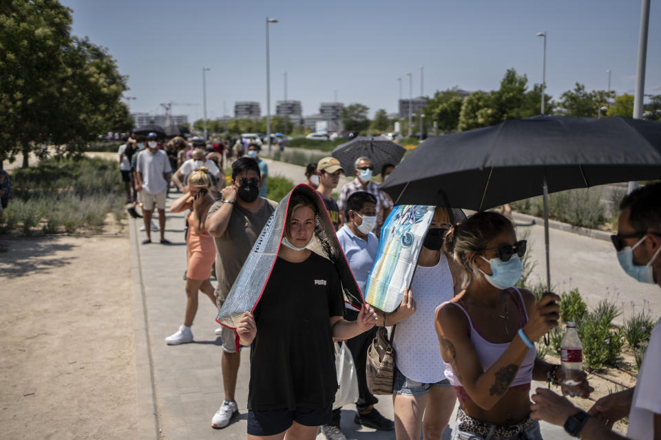 People protect themselves from the sun while waiting to be vaccinated against COVID-19 at the Isabel Zendal Hospital in Madrid, Spain, Tuesday, July 20, 2021. Spain is trying to stamp out a new wave of COVID-19 among its youth thanks to a robust vaccination program that is widely supported. Spain like the rest of the European Union got off to a slow start to compared to the United States and Britain when the first vaccines were released. But it has quickly made up ground once deliveries by drug makers started flowing. (AP Photo/Olmo Calvo)