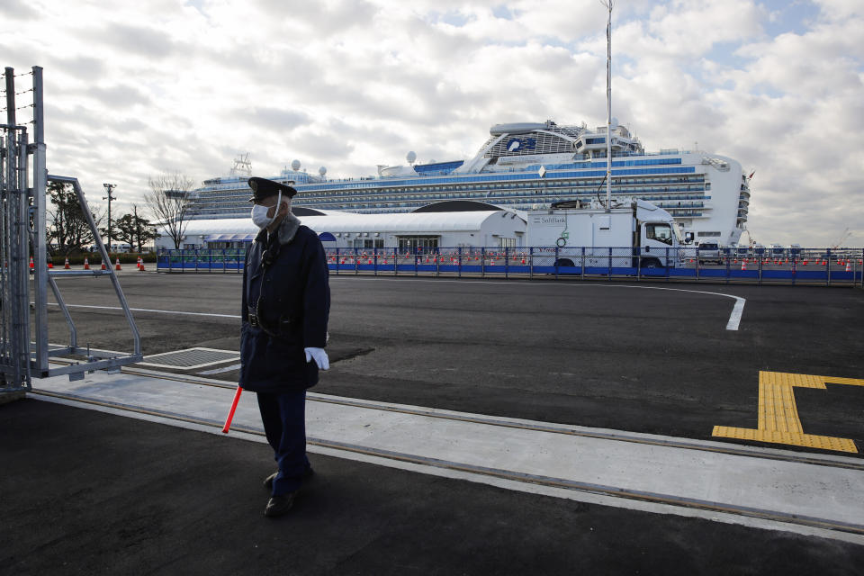 A security guard stands at the entrance to Yokohama port as the quarantined Diamond Princess cruise ship is seen in the background Wednesday, Feb. 19, 2020, in Yokohama, near Tokyo. Passengers tested negative for COVID-19 will start disembarking Wednesday. (AP Photo/Jae C. Hong)