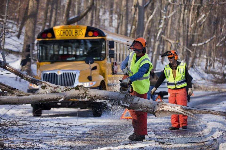 FILE - In this Friday, Feb. 7, 2014 file photo workmen clear a downed tree blocking a school bus in the aftermath of a winter storm, in Downingtown, Pa. Schools canceling classes because of winter weather in at least 10 states have used up the wiggle room in their academic calendars, forcing them to schedule makeup days or otherwise compensate for the lost time. (AP Photo/Matt Rourke, File)