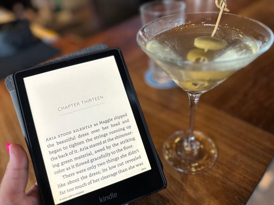 Terri holds a Kindle reader. To the left is a martini glass with two green olives on a toothpick skewer.