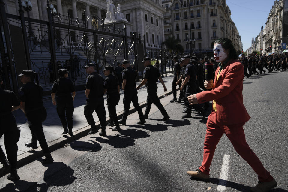 A protester in a Joker costume imitates a TV news reporter as he walks behind police leaving the area near Congress at the end of a protest against the economic and labor reforms proposed by Argentine President Javier Milei's government, during a national strike in Buenos Aires, Argentina, Wednesday, Jan. 24, 2024. (AP Photo/Rodrigo Abd)