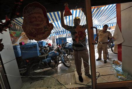 An employee pulls down the shutter of a Dominos Pizza outlet near a policeman (R) after it was ransacked by activists of Republican Party of India (RPI) in a Mumbai suburb December 20, 2013. REUTERS/Mansi Thapliyal