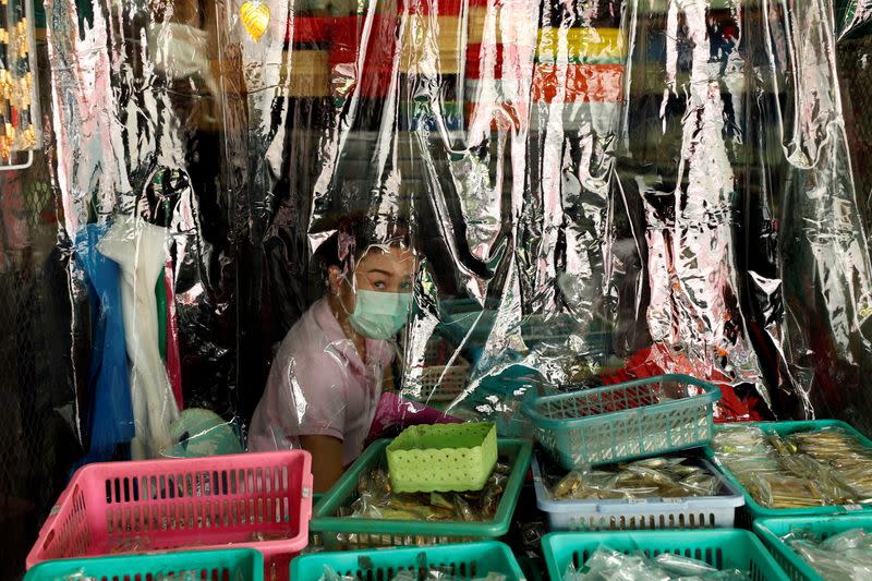 A shopkeeper is seen behind a protecting plastic curtain in Bangkok