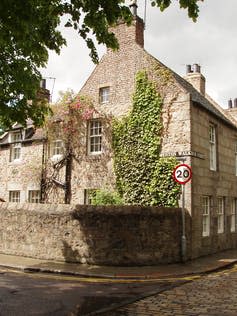 Stone house with ivy reaching up one wall to second story.