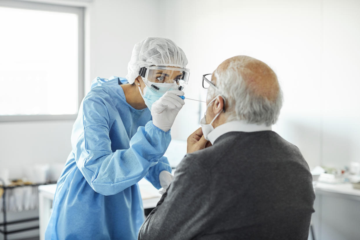 Female doctor in protective suit taking sample for swab test of senior man. Medical professional is examining elderly patient during COVID-19 crisis. They are in hospital.