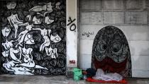 In this photo taken on Thursday Feb. 20, 2014, a homeless man sleeps next to work by 30-year-old Greek street artist Sonke in central Athens. The graphic arts graduate works as an art teacher in Athens and has street art ion Athens, Paris and Berlin. (AP Photo/Dimitri Messinis)