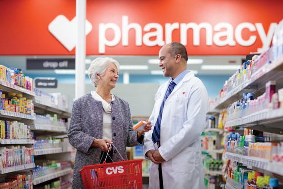 Older woman holding CVS basket standing next to a pharmacist in a CVS store.