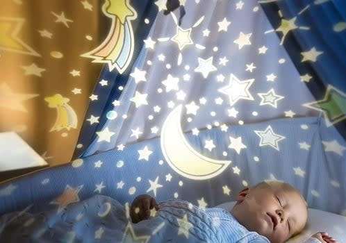 baby laying in crib with galaxy projection on the ceiling