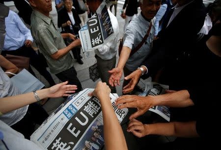 Passersby reach out to receive an extra edition of newspapers, which the headline reads "Britain, EU Leave", on the street in Tokyo, Japan, June 24, 2016. REUTERS/Issei Kato - RTX2HXAF