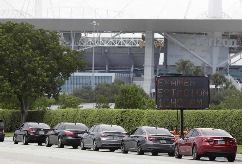 Cars line up next to a sign telling those waiting in Spanish to tune to, "Testing Station 1640 AM," for more information, Wednesday, Aug. 5, 2020, at a COVID-19 testing site outside Hard Rock Stadium in Miami Gardens, Fla. State officials say Florida has surpassed 500,000 coronavirus cases. Meanwhile, testing is ramping up following a temporary shutdown of some sites because of Tropical Storm Isaias. (AP Photo/Wilfredo Lee)