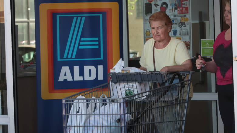 older woman leaving Aldi store with shopping cart