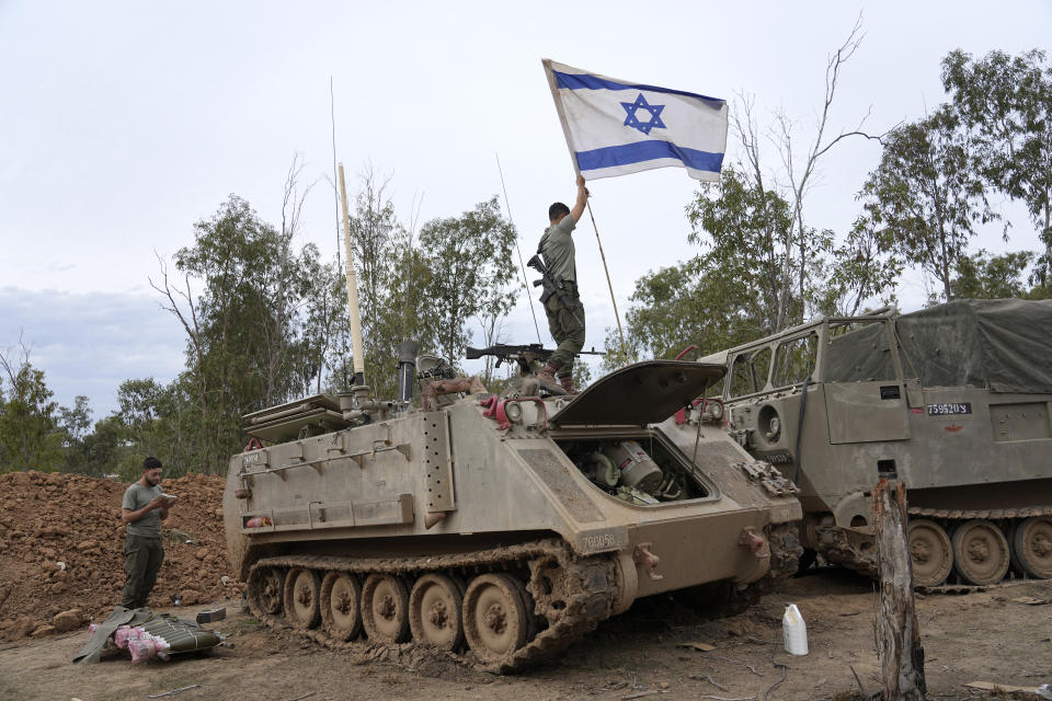 An Israeli soldier adjusts a national flag while another soldier prays near the Israel-Gaza border in southern Israel, Saturday, Nov. 25, 2023. Hamas was preparing to release more than a dozen hostages Saturday for several dozen Palestinian prisoners held by Israel, part of an exchange on the second day of a cease-fire. AP Photo/Tsafrir Abayov)