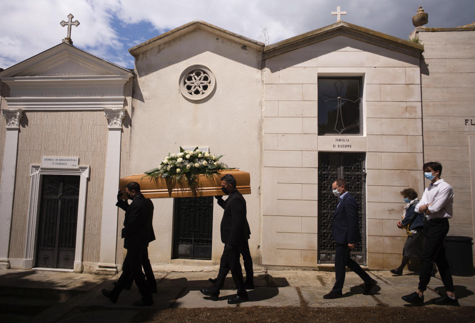 FILE - In this May 12, 2020 file photo, the casket containing the body of Annunziata Ginoble, the mother of Mayor of Roseto degli Abruzzi Sabatino Di Girolamo, third from right, with his sister, Marisa Di Felice, second from right, and his son, Francesco, right, is taken to her burial site inside the small cemetery of Montepagano, central Italy. Italy is poised to reclaim the dishonor of reporting the most coronavirus deaths in Europe, as the second surge ravages the country’s disproportionately old population and exposes how public health shortfalls and delayed restrictions compounded a lack of preparedness going into the pandemic. (AP Photo/Domenico Stinellis, file)