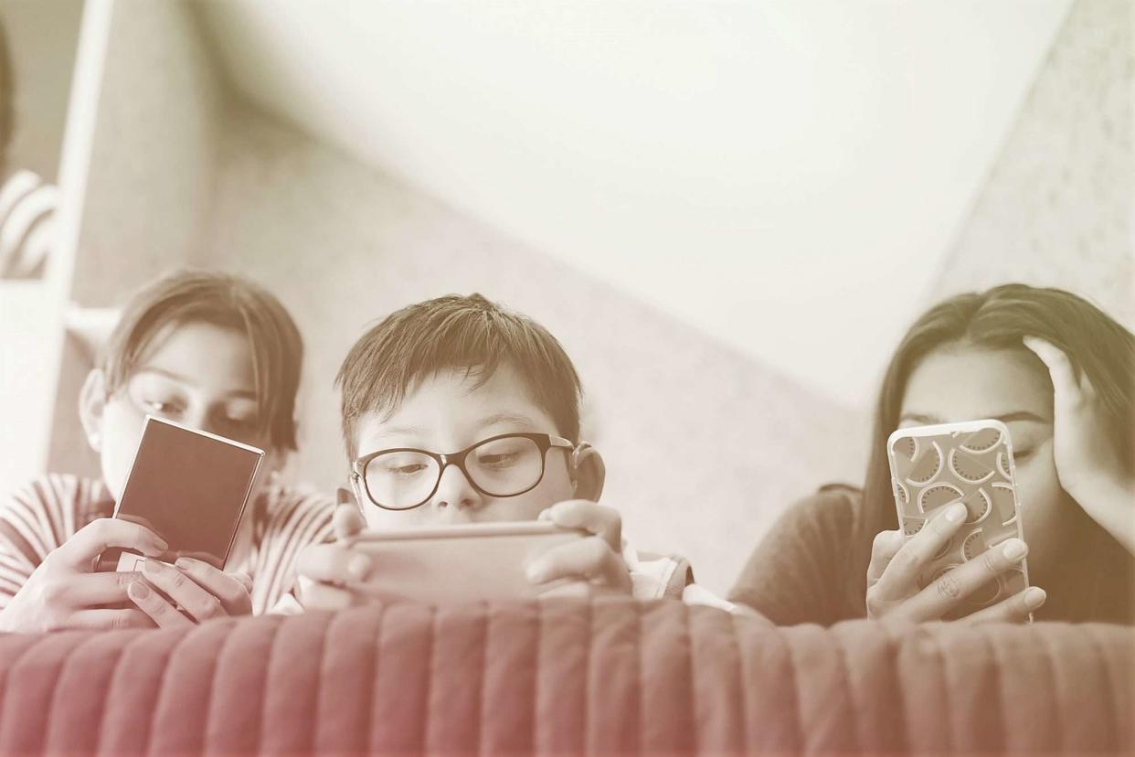 low angle view of three kids laying down looking at their cell phones