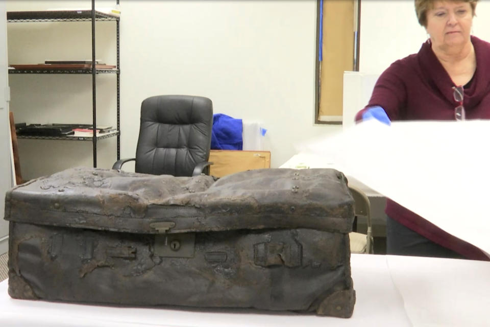 In this Tuesday, Feb. 18, 2020 image taken from video, Alexandra Klingelhofer, executive director for collections at RMS Titanic, Inc., lifts a paper sheet off of a trunk recovered from the ship's wreckage at the company's storage facility in Atlanta. RMS Titanic, Inc., the salvage firm that has plucked silverware, china and gold coins from the ship's wreckage, is now hoping to recover the so-called "voice" of the doomed ocean liner: The Marconi Wireless Telegraph Machine that had broadcast its increasingly frantic distress calls. (AP Photo/Angie Wang)