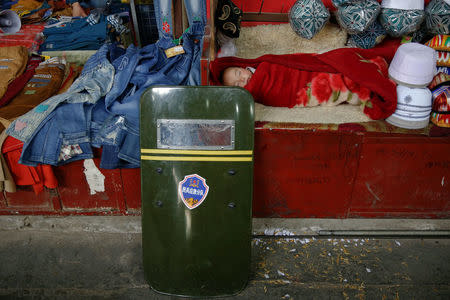 A child sleeps as a riot shield leans on a stall at the bazaar in Hotan, Xinjiang Uighur Autonomous Region, China, March 21, 2017. REUTERS/Thomas Peter