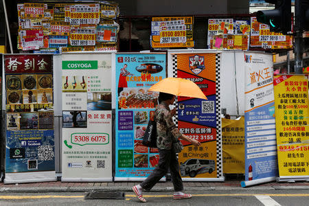 A woman walks past banners promoting retail goods and services displayed in front of closed shops for rent at the shopping Mongkok District in Hong Kong, China August 29, 2016. REUTERS/Bobby Yip/Files