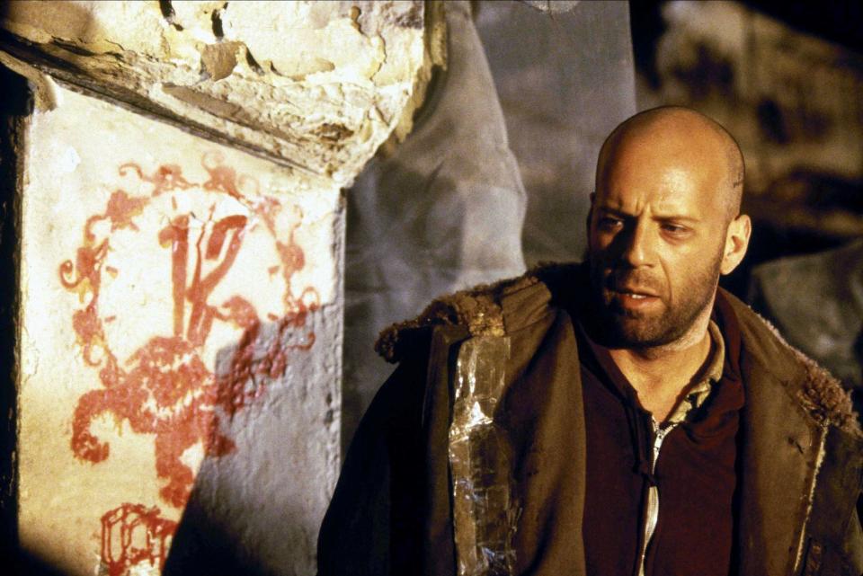 Bruce Willis stands by some strange street art in a post-apocalyptic future in “Twelve Monkeys”