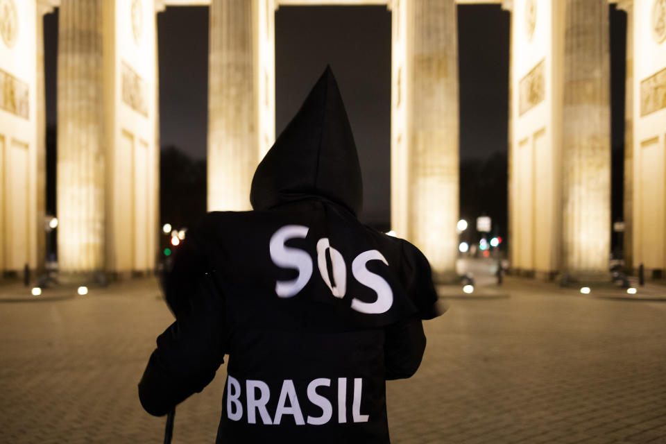 Brazilian activist and artist Rafael Puetter, dressed as the grim reaper, walks in front of the Brandenburg Gate in a one-man protest through Berlin, Germany, early Wednesday, April 7, 2021. The multimedia artist starts his performance at the Brazilian embassy in Berlin at midnight every night to protest against Brazil's COVID-19 policies. Rafael Puetter walks to the Brandenburg Gate and then to the nearby German parliament building, in front of which he counts out a sunflower seed to represent each of the lives that were lost over the past 24 hours in Brazil because of the coronavirus pandemic. (AP Photo/Markus Schreiber)