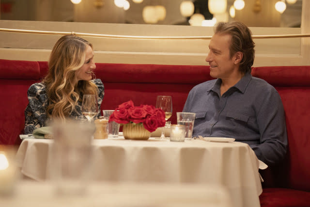 Carrie and Aidan smile at each other as they sit at a restaurant dinner table
