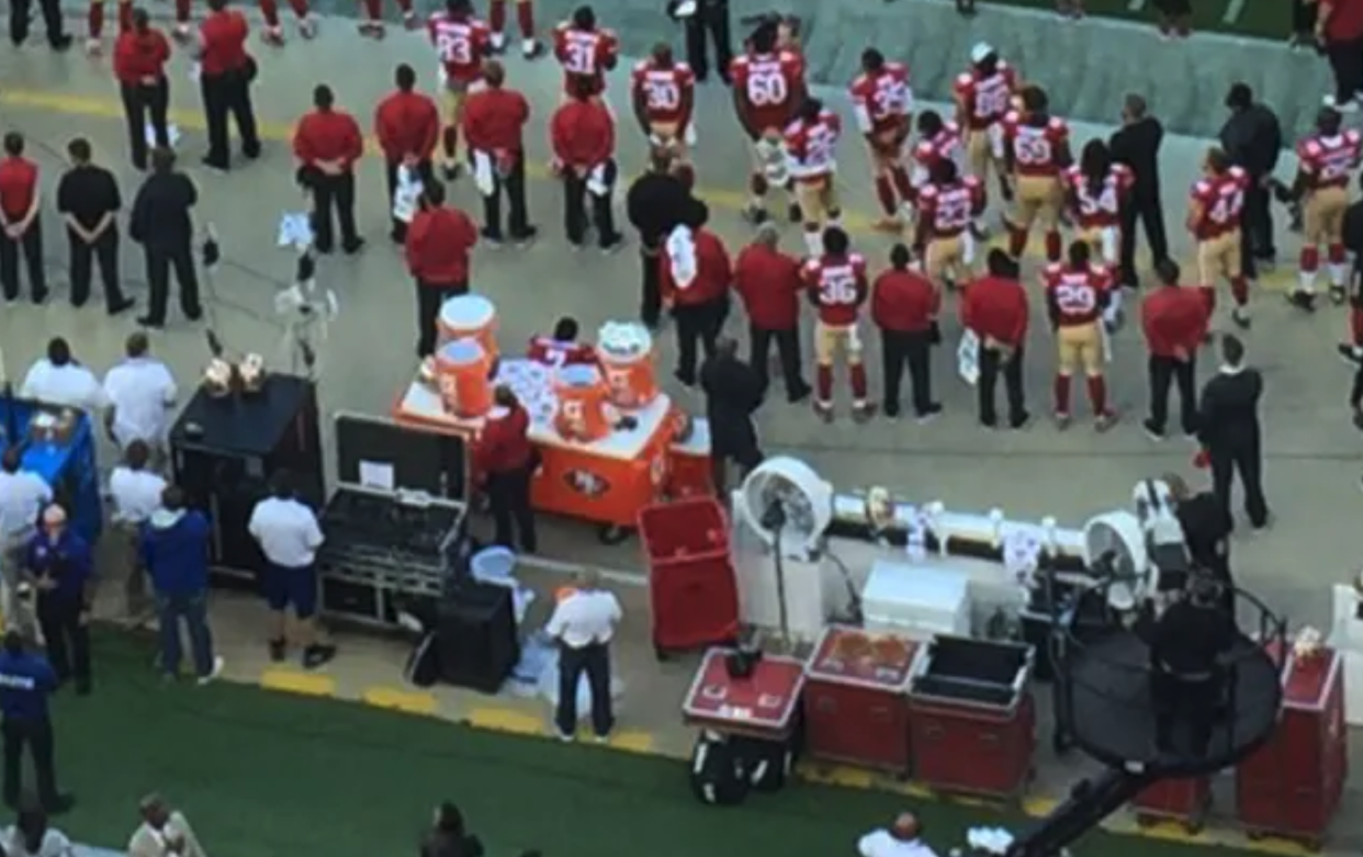 NFL quarter-back Colin Kaepernick (pictured centre), sat down as everyone else stood on 26 August, 2016, in a gesture which would go on to inspire a global movement. (Twitter/Jennifer Lee Chan/SB Nation)