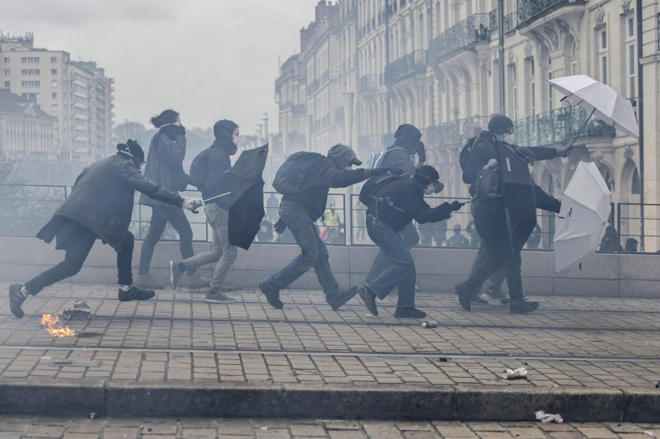 Protesters shield with umbrellas as they scuffle with riot police during rally in Nantes, western France, Thursday, March 23, 2023. French unions are holding their first mass demonstrations Thursday since President Emmanuel Macron enflamed public anger by forcing a higher retirement age through parliament without a vote. (AP Photo/Jeremias Gonzalez)