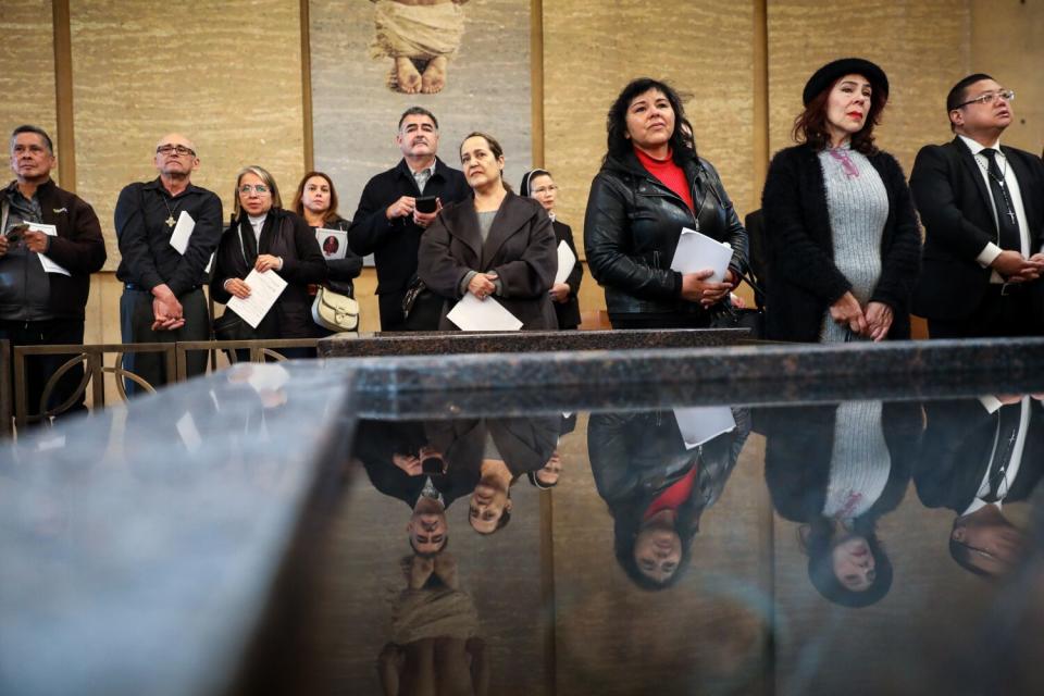 Visitors are reflected in the baptismal font as they wait