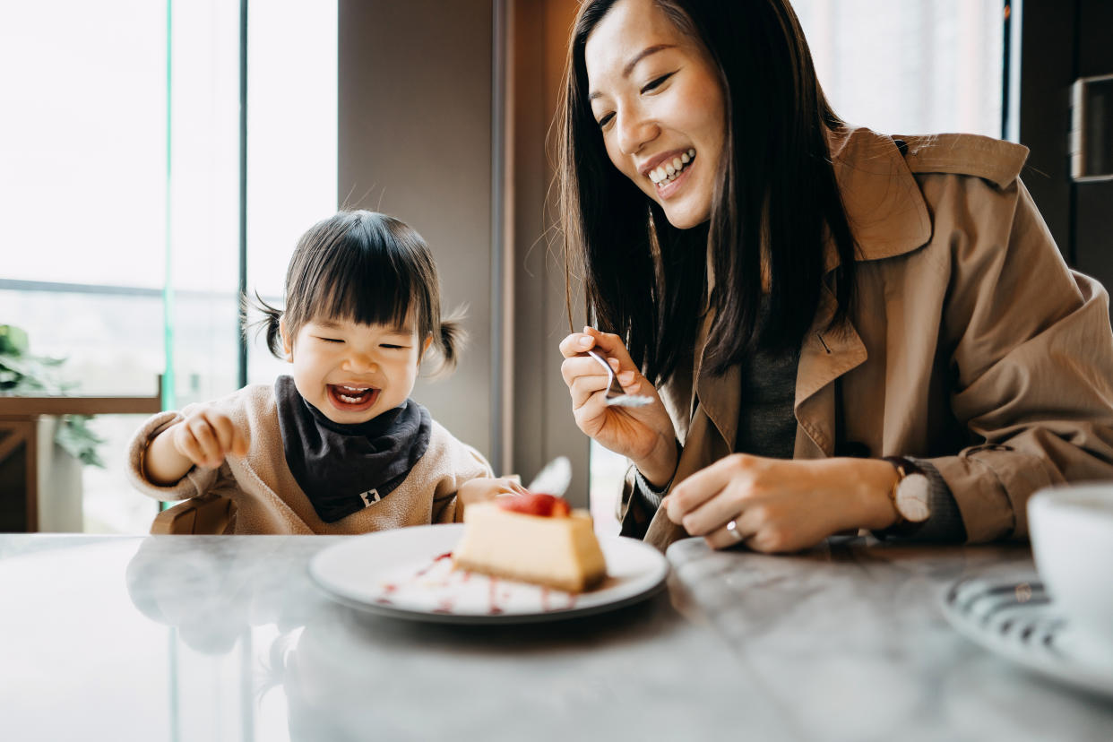 Mother and little daughter sharing a piece of cake in the cafe, both of them are smiling joyfully