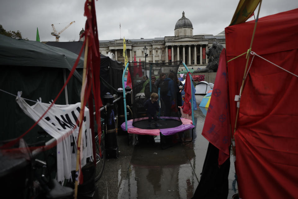 A child plays on a trampoline setup alongside Extinction Rebellion climate change protester tents in Trafalgar Square, London, Friday, Oct. 11, 2019. Some hundreds of climate change activists are in London during a fifth day of protests by the Extinction Rebellion movement to demand more urgent actions to counter global warming. (AP Photo/Matt Dunham)