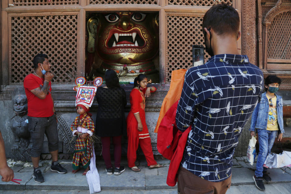 A Nepalese girl stands for a photograph in front of an idol of Swet Bhairav statue while participating in a procession to mark 'Gai Jatra', or cow festival, in Kathmandu, Nepal, Aug. 4, 2020. The festival is celebrated by the Newar community in memory of deceased family members who died the preceding year, believing that the cow will guide them in their journey to heaven. (AP Photo/Niranjan Shrestha)