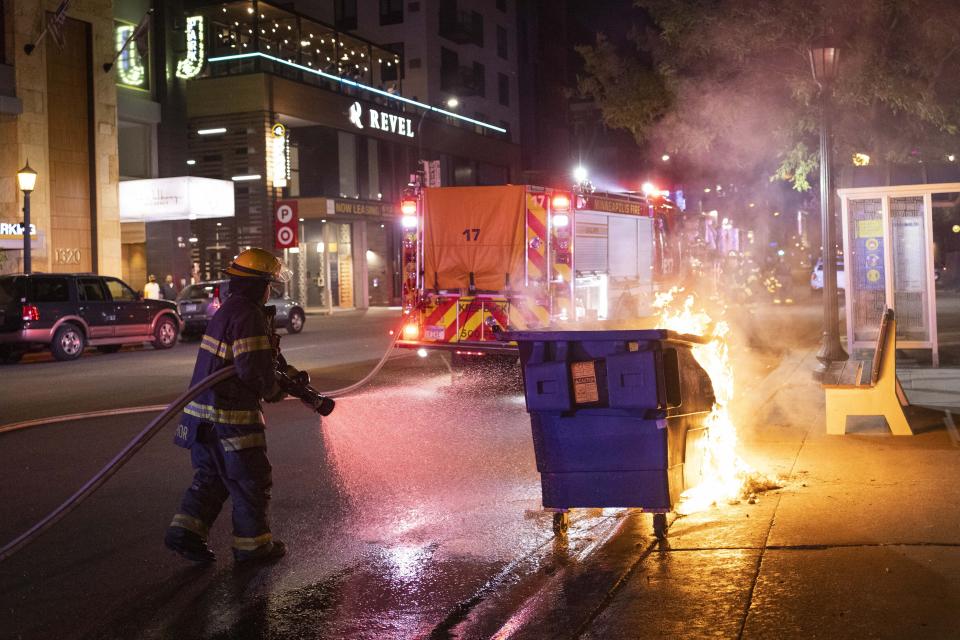 A firefighter puts out a dumpster fire after protesters clash with police following a vigil that was held for Winston Boogie Smith Jr. early in on Saturday, June 5, 2021. Authorities said Friday that a man wanted on a weapons violation fired a gun before deputies fatally shot him in Minneapolis, a city on edge since George Floyd's death more than a year ago under an officer's knee and the more recent fatal police shooting of Daunte Wright in a nearby suburb. (AP Photo/Christian Monterrosa)