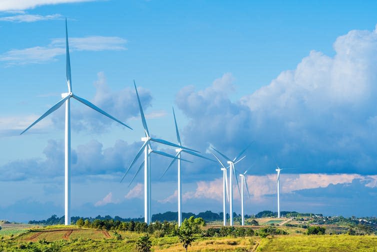 A wind farm on green fields against a cloudy sky.