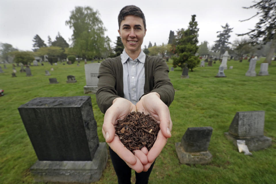 FILE - In this April 19, 2019, file photo, Katrina Spade, the founder and CEO of Recompose, a company that hopes to use composting as an alternative to burying or cremating human remains, poses for a photo in a cemetery in Seattle, as she displays a sample of compost material left from the decomposition of a cow using a combination of wood chips, alfalfa and straw. On Tuesday, May 21, 2019, Washington Gov. Jay Inslee signed a bill into law that allows licensed facilities to offer "natural organic reduction," which turns a body, mixed with substances such as wood chips and straw, into soil in a span of several weeks. Th law makes Washington the first state in the U.S. to approve composting as an alternative to burying or cremating human remains. (AP Photo/Elaine Thompson, File)