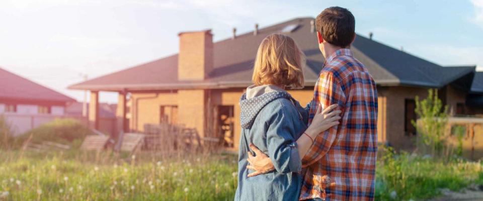 Back view of happy family is standing near their new modern house and hugging